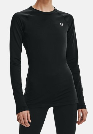 Frau trägt eng anliegendes, langärmeliges schwarzes Sportoberteil mit Under Armour-Logo auf der Brust und passende schwarze Leggings.