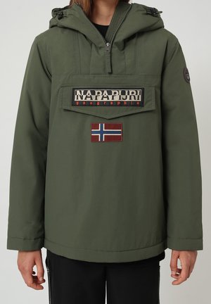 Persona che indossa una giacca con cappuccio verde oliva con tasca frontale etichettata "Napapijri geographic" e toppa della bandiera norvegese sotto.