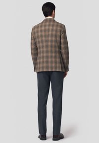 Brązowa marynarka w kratę o klasycznym kroju, zestawiona z ciemnoszarymi spodniami. Teksturowana tkanina z detalicznym przeszyciem i akcentami guzików.