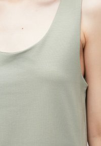 Lysegrønn singlet laget av teksturert stoff. Har bred halslinning og er ermeløs, viser deler av skulderen og brystet.