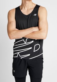 Czarny sportowy top na ramiączkach z geometrycznym białym wzorem, wykonany z lekkiego materiału. Nosi się go z czarnymi szortami, które mają logo Under Armour.