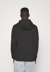 Felpa nera con cappuccio, dal texture morbido, con una vestibilità rilassata e tasca a marsupio, abbinata a jeans in denim blu chiaro.