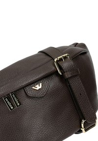 Bruine leren schoudertas met textuur, voorzien van een logo met gouden accenten, een verstelbare schouderband en een bovenklep sluiting. Voorzien van metalen hardwaredetails.