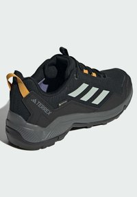 Zapatos de senderismo negros con acentos grises y reflectantes, que presentan una parte superior texturizada, detalles en naranja y una suela duradera para tracción.