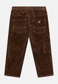 Pantalones de pana marrones con estrías verticales, cinco bolsillos y un parche cuadrado con el logo en la parte trasera. Presentan un diseño de pierna recta.