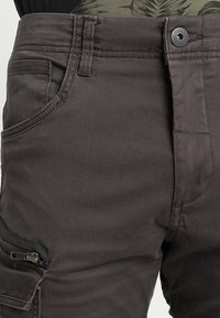 Dunkelgraue Cargo-Hosen aus einem strukturierten Stoff, mit Fronttaschen, einer seitlichen Reißverschlusstasche und einem Knopfverschluss.