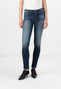 Fekete koptatott farmer skinny farmernadrág, öt zsebes, közepes derékkal. Magassarkú fekete cipővel párosítva.