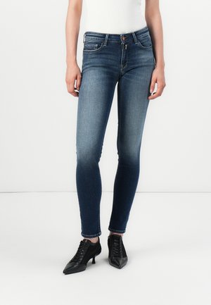 Schmale Jeans aus dunkelblauem Denim mit leichter Ausbleichung. Sie verfügen über ein Fünf-Taschen-Design und eine mittelhohe Taille. Kombiniert mit schwarzen, Absatzschuhen.