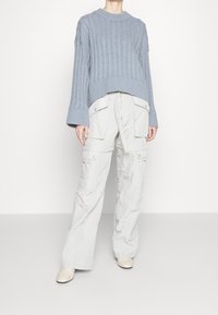 Maglione a coste di un azzurro chiaro con maniche larghe abbinato a pantaloni cargo grigi chiari con più tasche e un fit rilassato.