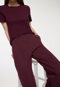 Burgundowa koszulka z okrągłym dekoltem i krótkimi rękawami, zestawiona z dopasowanymi spodniami typu tapered, które mają boczne kieszenie i gładką fakturę.