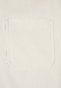 Quadratische weiße Stofftasche mit sichtbaren Nähten auf weißem, geripptem Textilhintergrund.