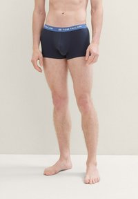 Boxers bleus foncés avec une taille élastique douce portant l'étiquette "TOM TAILOR". Le tissu semble lisse et ajusté, avec un design de poche contournée.