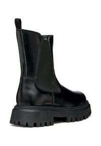 Botín de piel negra hasta el tobillo con panel lateral elástico, asa de tirón y suela gruesa con dibujo, mostrado desde el lado exterior.