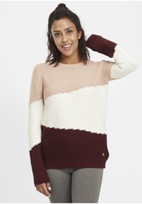 Pull en tricot avec un design rayé en rose poussiéreux, crème et bordeaux. Texture côtelée avec un col rond et des poignets allongés.
