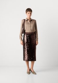 Smeđa bluzica sa dugim rukavima i dugmadi kombinirana sa smešnim pencil suknjama ukrašenim šljokicama. Outfit upotpunjuju metalik štikle s oštrim vrhom.