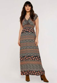 Maxikleid mit V-Ausschnitt, kurzen Kappärmeln, schwarzem Grund, floralen Mustern in Rot, Pink und Weiß sowie einer taillierten Taille, kombiniert mit braunen Stiefeln.