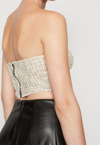 Top bez ramiączek ozdobiony koralikami, z fakturowanym kremowym materiałem i zamkiem z tyłu, zestawiony z czarną skórzaną spódnicą.