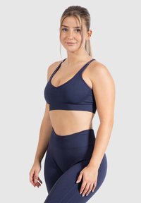 Sujetador deportivo azul marino con tirantes ajustables, tejido texturizado y diseño de escote en V, combinado con leggins de cintura alta del mismo color.