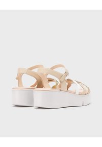 Sandalias de plataforma beige con un upper texturizado, que cuentan con múltiples tiras entrecruzadas y una suela blanca. Detalle de hebilla ajustable en el tobillo.