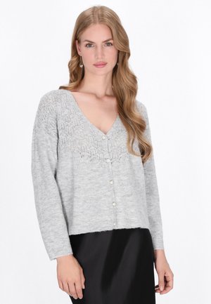 Cardigan gri tricotat cu decolteu în V, având un model de dantelă pe partea superioară, închidere cu nasturi și mâneci lungi. Margină dreaptă.