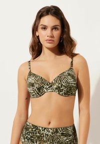 Bikiniöverdel i ett grönt och brunt tropiskt bladmönster, med djup V-ringning, justerbara axelband och mjukt tyg.