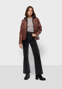 Giacca di pelle marrone con cappuccio grigio, chiusura con zip e tasche frontali. Abbinata a jeans neri a vita alta svasati e stivali neri massicci.