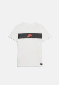 Weißes T-Shirt mit kurzen  Ärmeln, einem schwarzen horizontalen Streifen über der Brust und einem roten Nike-Logo, das mittig auf dem Streifen platziert ist.