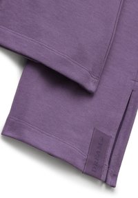 Gros plan sur un tissu violet plié, avec un ourlet cousu et une petite étiquette cousue portant la mention "DREAM 9x" près d'une fente sur le côté.
