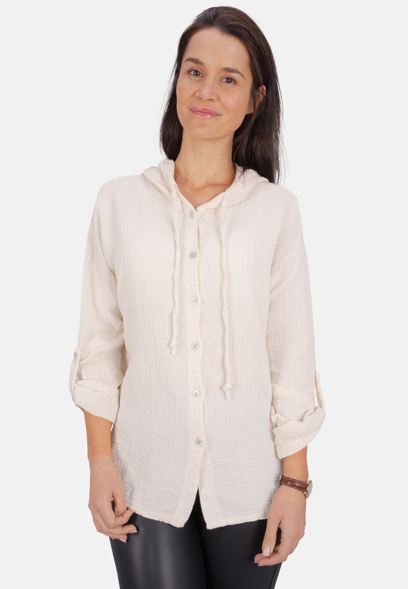 Hellbeige, knöpfbares Hemd mit Kapuze. Aus strukturiertem Stoff gefertigt, mit hochrollbaren Ärmeln und Fronttaschen. Silberfarbene Knöpfe.