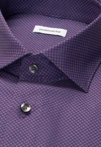 Chemise habillée à col avec un petit motif géométrique bleu et violet et deux boutons foncés, montrant une étiquette blanche avec le nom de la marque seidensticker.
