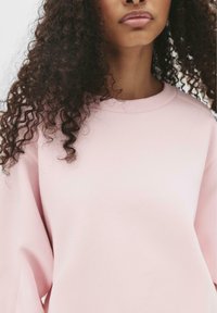 Felpa rosa chiaro con scollo rotondo e tessuto morbido e strutturato. Presenta una vestibilità comoda e maniche lunghe.