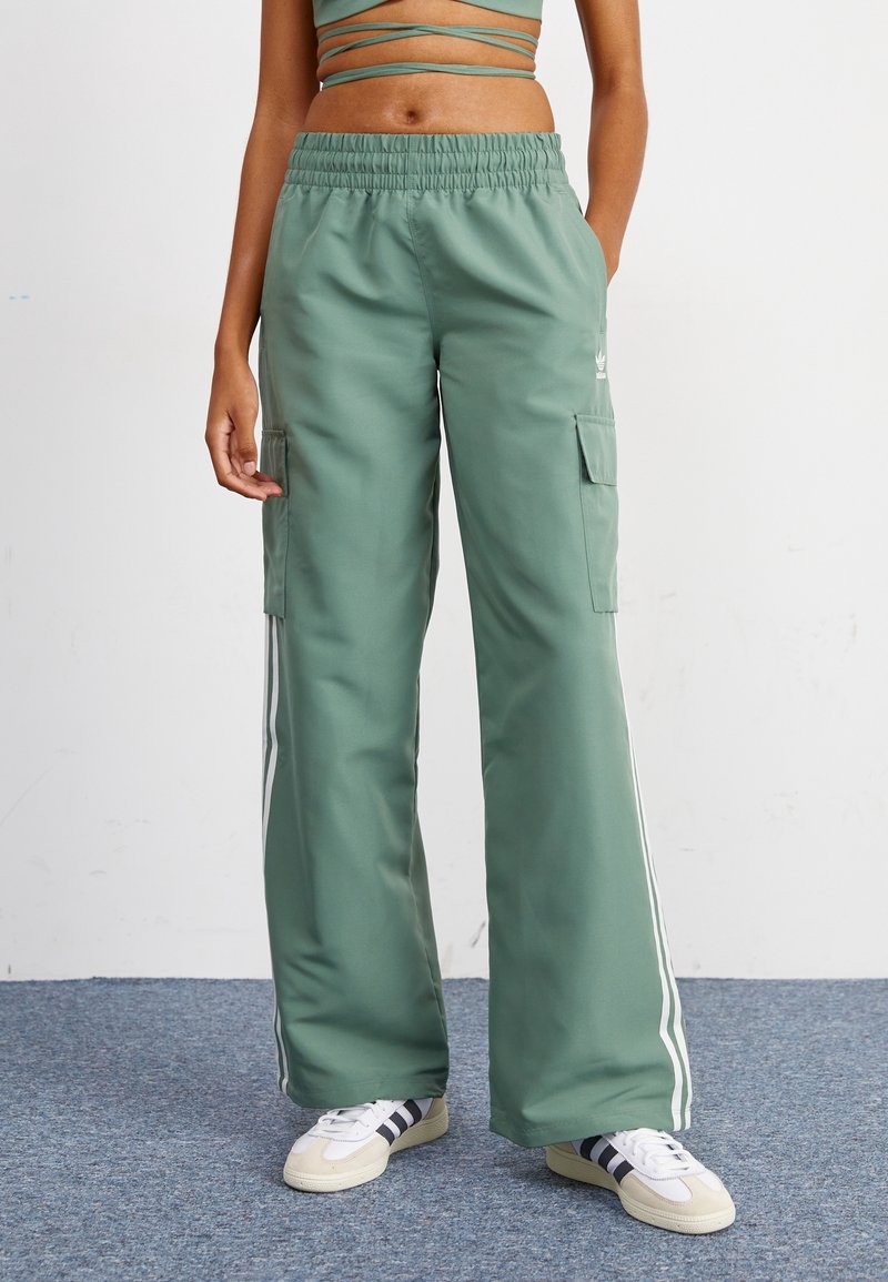 Grüne Cargo-Hosen mit weitem Bein, elastischem Taillenbund, Seitentaschen und weißen Streifen an den Seiten. Glatte Textur mit lässigem Design.