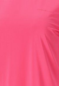 Pink atletisk skjorte lavet af letvægts, åndbart stof. Har et struktureret mønster og et diskret mærkelogo trykt på brystet.