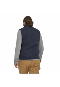 Chaleco de forro polar azul con cuello alto, usado sobre una camiseta de manga larga gris claro y pantalones beige. Textura suave, diseño informal y sin cierres visibles.