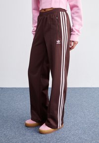 Ruske sweatpantsit, joissa on valkoiset kolmoispinnat sivuilla, sisältää vetoketjullisen taskun ja Adidaksen logon edessä. Tasainen vyötärönauhan muotoilu.