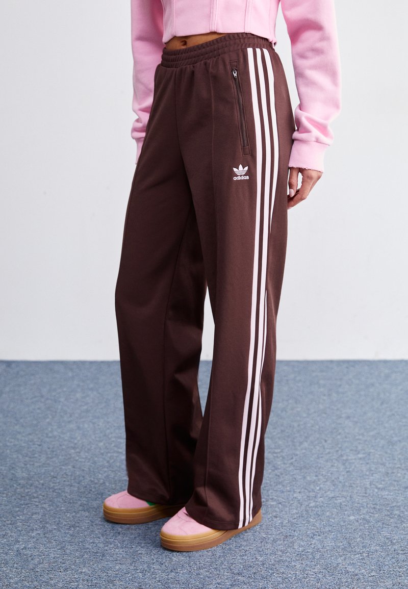 Ruske sweatpantsit, joissa on valkoiset kolmoispinnat sivuilla, sisältää vetoketjullisen taskun ja Adidaksen logon edessä. Tasainen vyötärönauhan muotoilu.