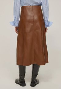 Gonna midi in pelle marrone con texture liscia, design svasato e dettagli di cucitura. Abbinata a una camicia a righe blu chiaro e stivali neri al ginocchio.