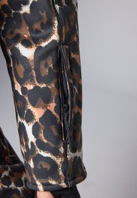 Topp med leopardmønster til trening, med en tettsittende design, glidelåslomme på siden og en glatt tekstur i brune, svarte og beige farger.