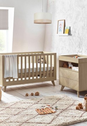 Wooden baby crib and changing table in bright nursery with toys, soft rug, framed rainbow prints, and hanging light fixture.