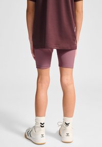 Bordeaux T-shirt met zwarte afwerking, aansluitende roze shorts en witte schoenen met zwarte accenten en logo. Witte sokken met zwarte patronen.