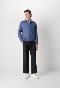 Svetlo modra zip-up jakna s ravnim ovratnikom, elastičnimi manšetami in črnimi hlačami. Obleka je dopolnjena z belimi teniskami.