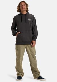 Felpa grigia scura con tasca frontale, cappuccio regolabile con stringhe e un piccolo logo. Abbinata a pantaloni cargo verde oliva chiaro e sneakers scure.