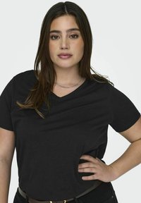 T-shirt noir à col en V en tissu doux et lisse. Manches courtes, coupe décontractée et détails de couture visibles. Porté avec une ceinture.