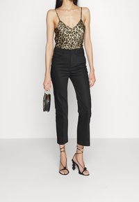 Camisola con stampa leopardata e spalline sottili, pantaloni neri su misura e tacchi neri con cinghie e dettagli in perline, mentre tiene una piccola borsa rotonda.