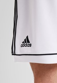 Pantalones cortos deportivos blancos con acentos negros, que presentan un logotipo de Adidas bordado en negro y ribetes negros contrastantes a lo largo de los lados.