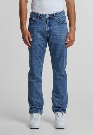 Blauwe denim spijkerbroek met een rechte pasvorm, voorzien van vijf zakken en een knoopsluiting, gecombineerd met witte sneakers.