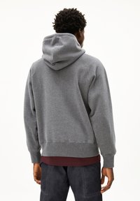 Grijze capuchontrui gemaakt van zachte stof, met een ontspannen pasvorm, ribgebreide manchetten en zoom, met een bordeauxrode onderkant die zichtbaar is.