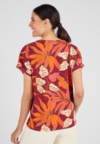 Top a maniche corte color bordeaux con motivi floreali colorati. Presenta fiori arancioni e rosa con dettagli crema e risvolti sulle maniche.