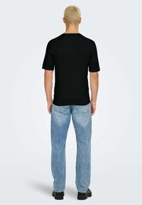 T-shirt nera a maniche corte con colletto tondo, realizzata in morbido cotone. Abbinata a jeans in denim blu chiaro e scarpe nere.