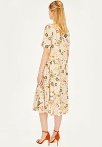 Beżowa sukienka w kwiatowy wzór z krótkimi rękawami, dopasowaną talią i zwiewnym dołem. Połączona z pomarańczowymi zamszowymi szpilkami.